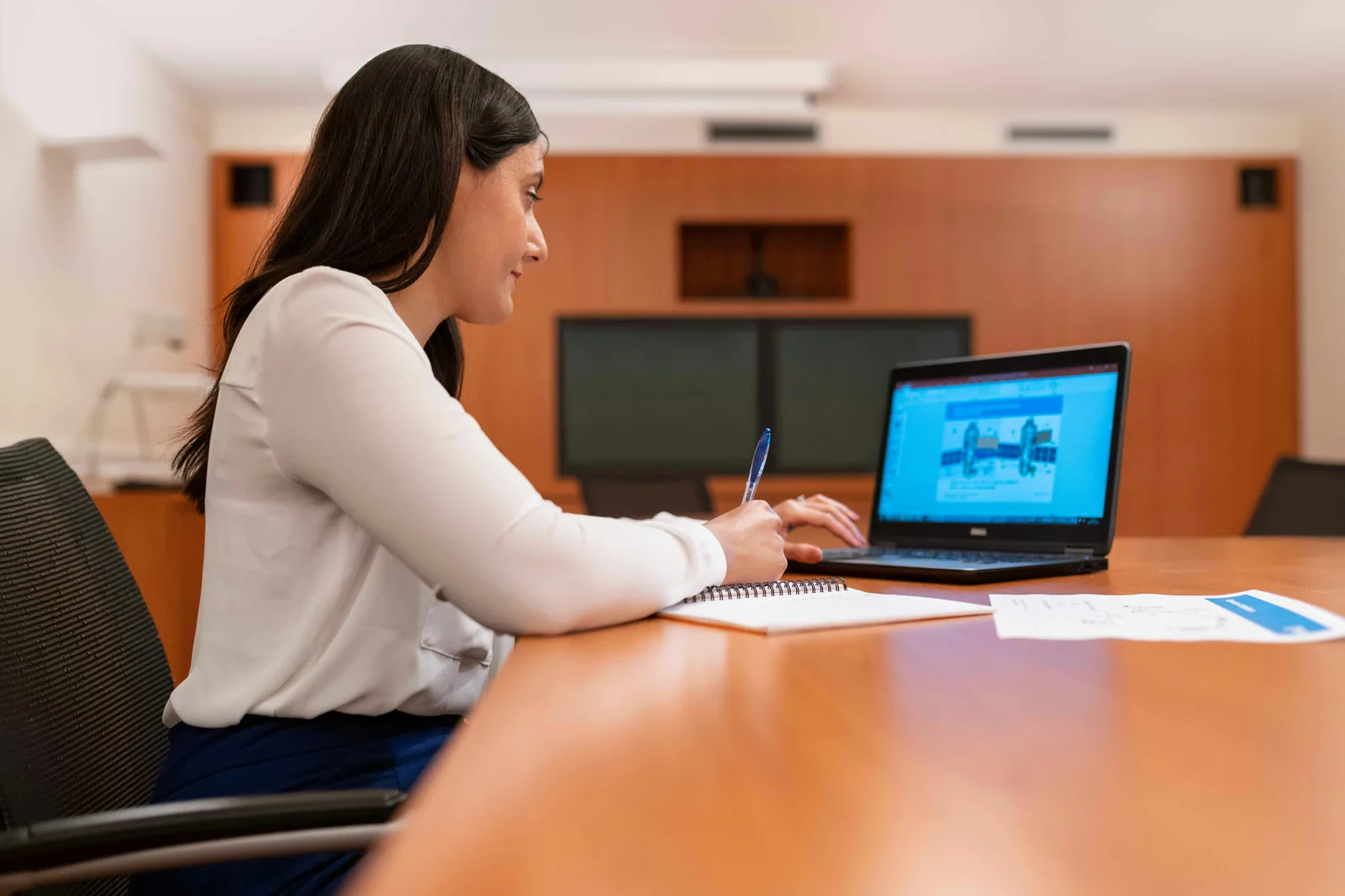 Woman taking notes beside a laptop at a conference table
