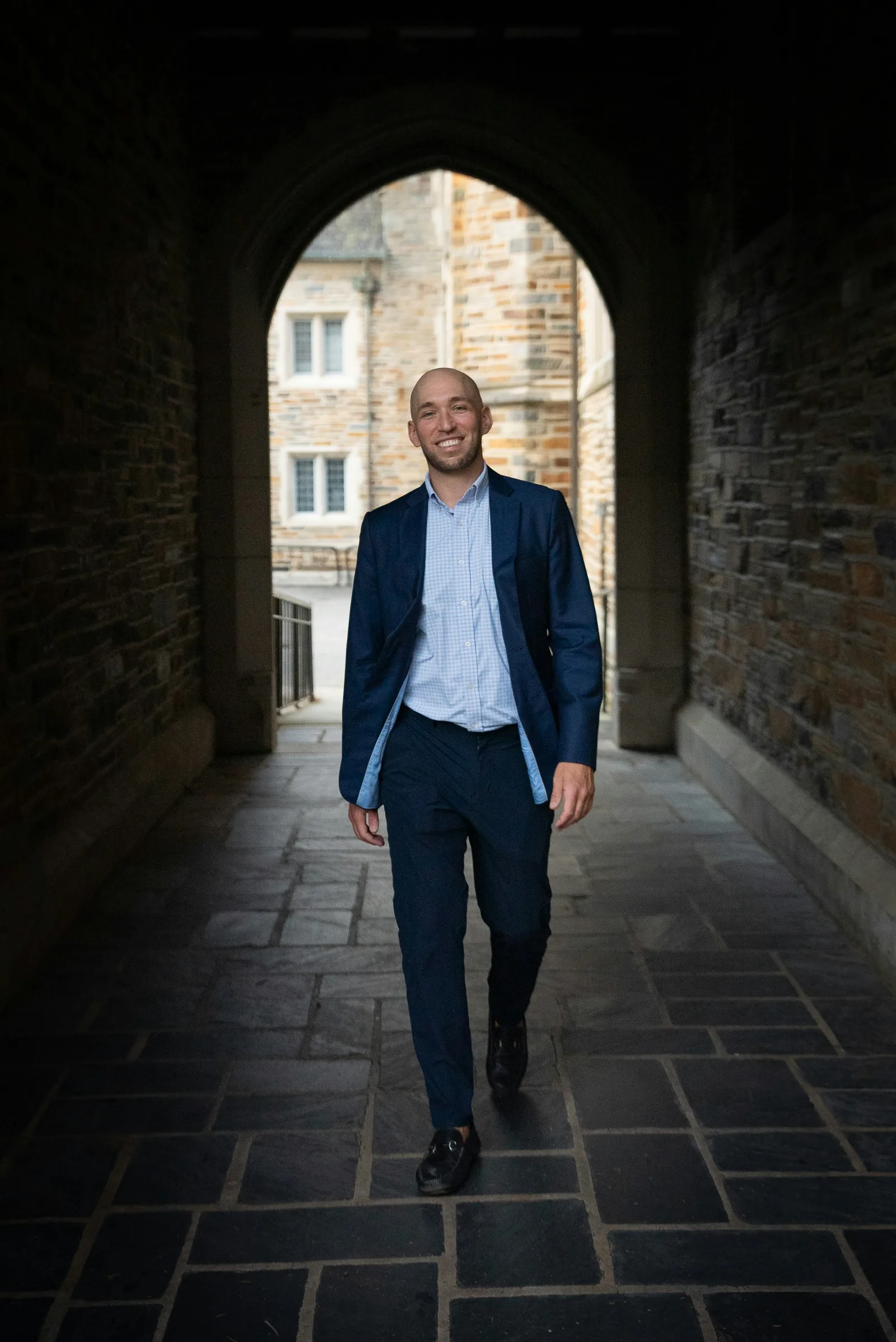 Smiling man in a navy suit walking through a stone archway