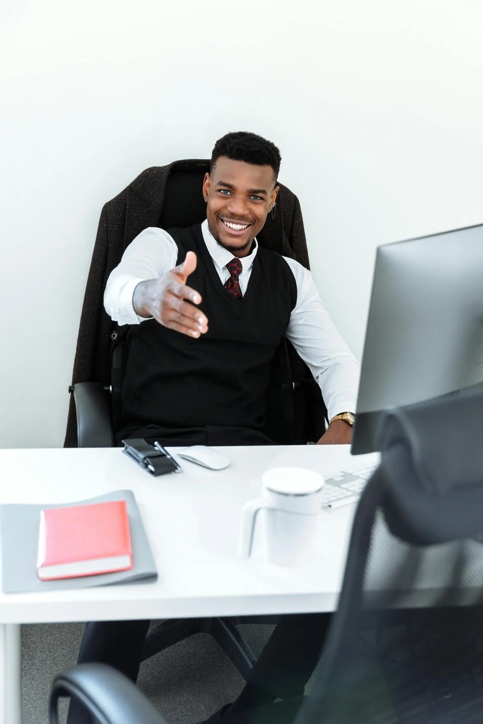 Smiling man at an office desk reaching out to shake hands