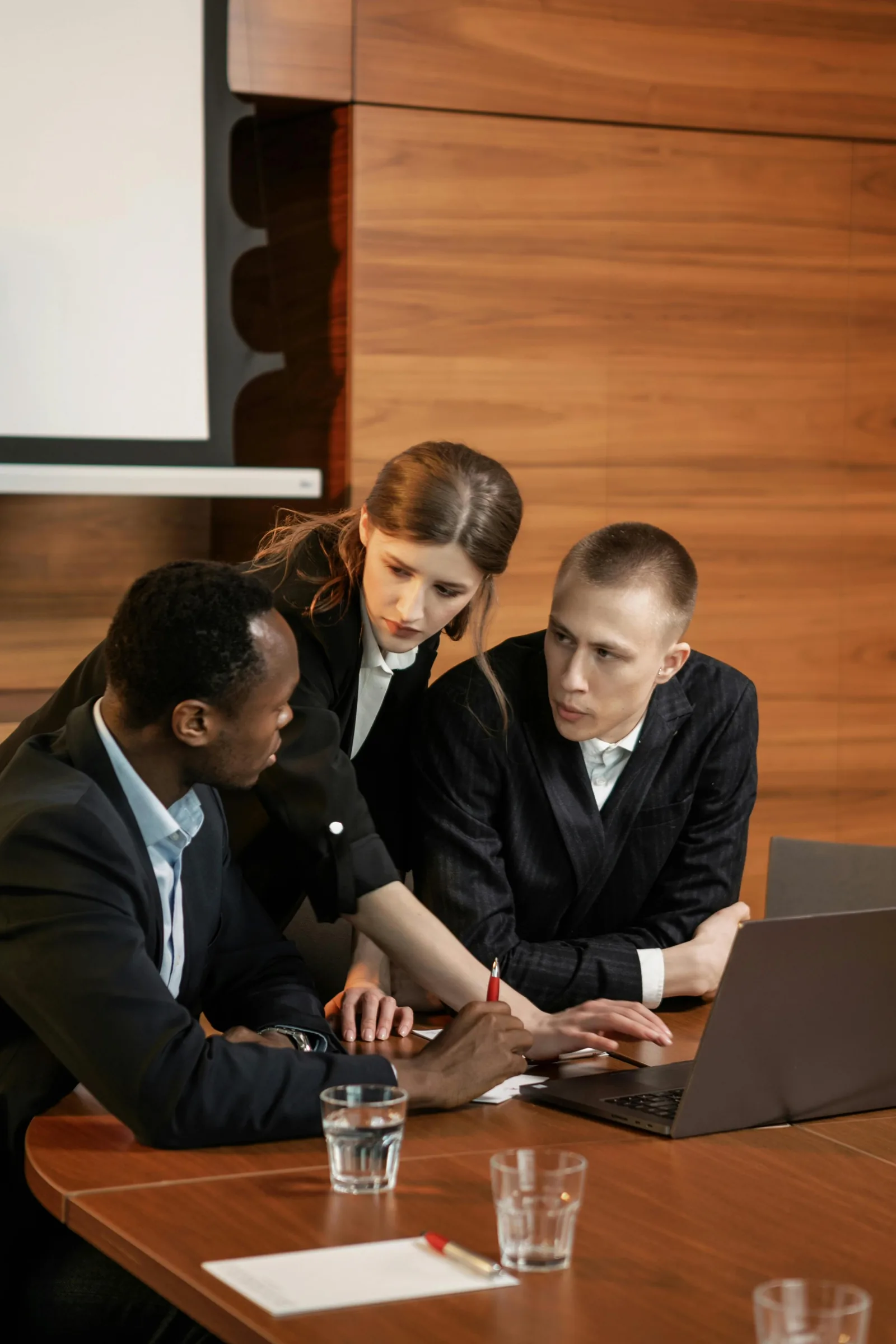 Three colleagues in suits looking at a laptop at a conference table