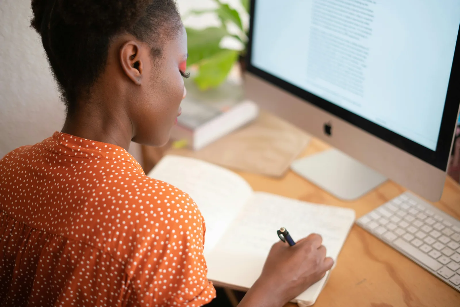 Woman taking notes in a notebook beside a desktop computer