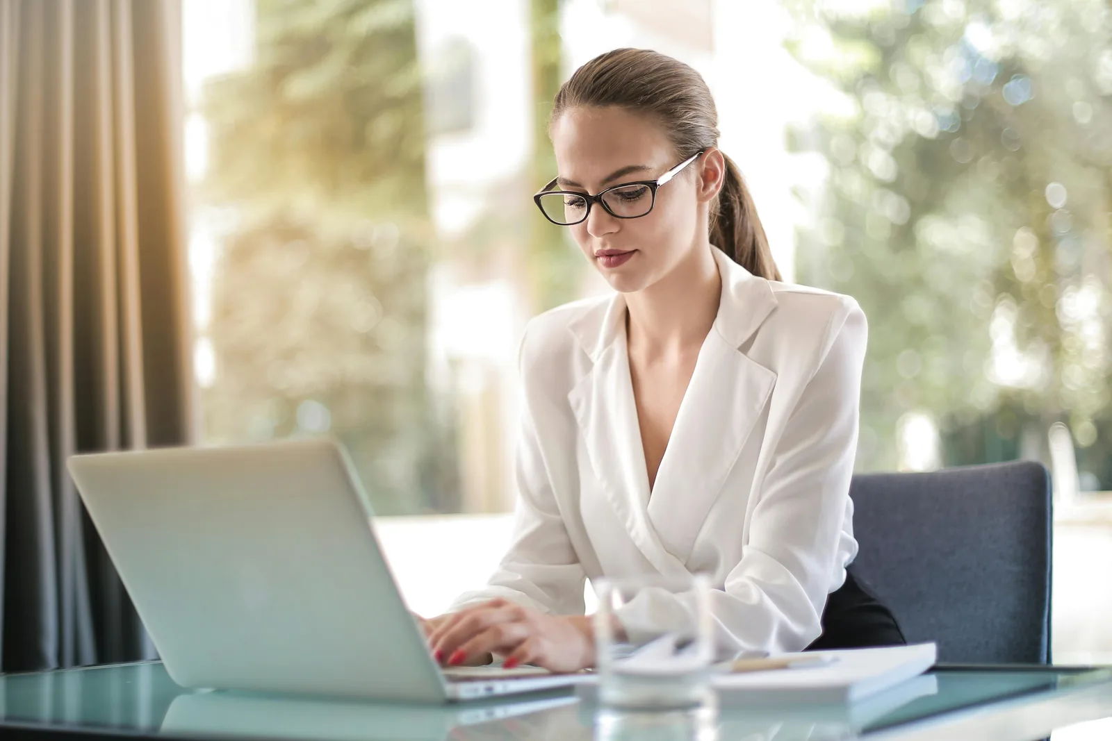 Woman in glasses and a white blouse typing on a laptop